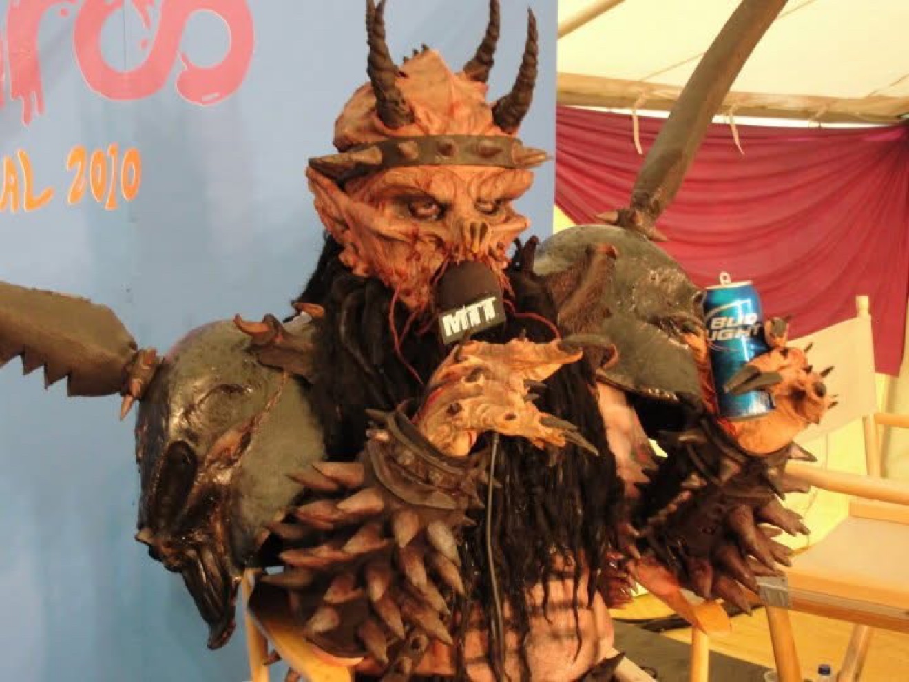 Dave Brockie as Oderus Urungus of GWAR holding the Moe Train's Tracks mic and a beer in front of the Bonnaroo 2010 backdrop