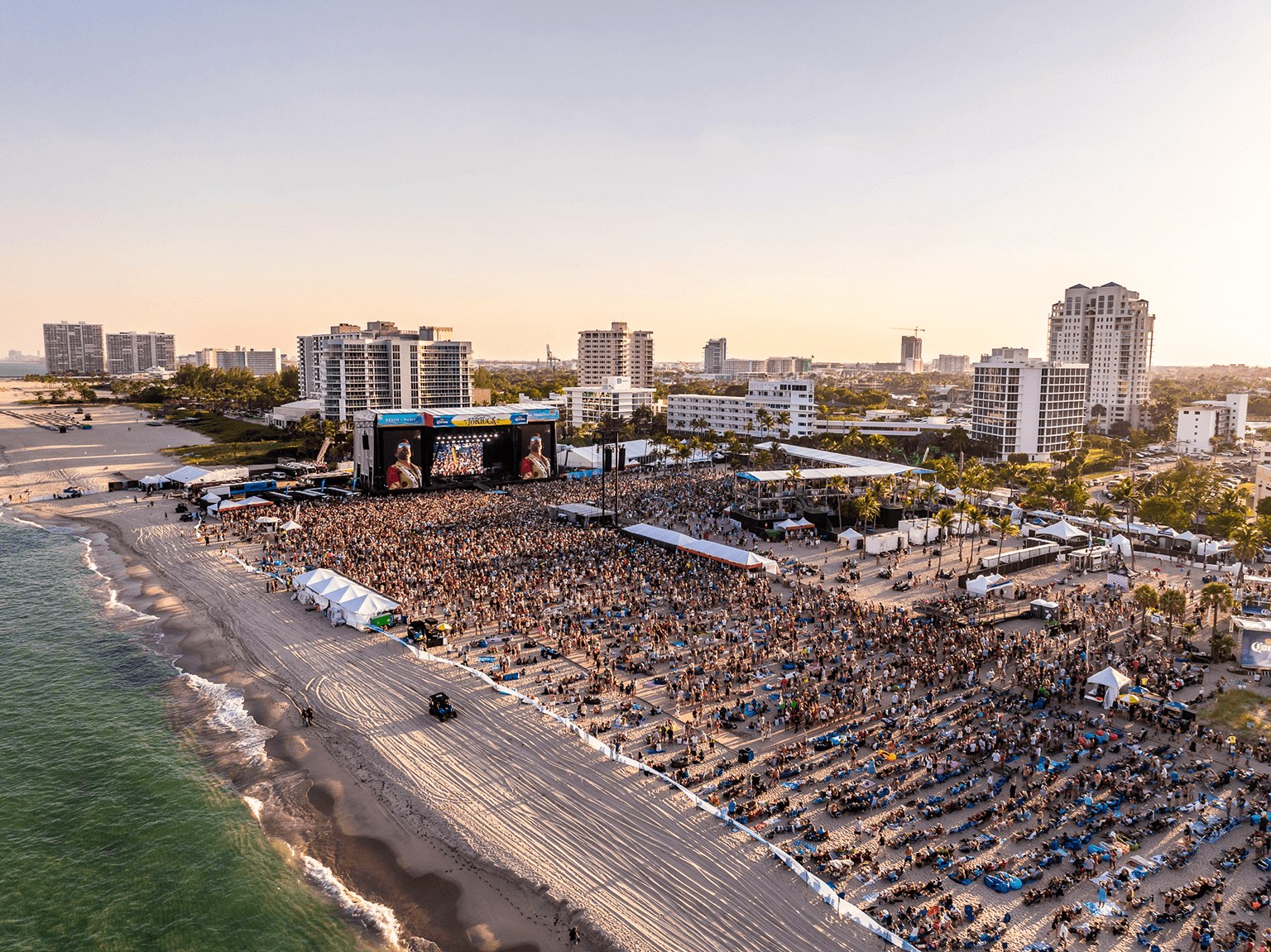 Golden hour over Fort Lauderdale Beach, the Tortuga crowd spread across the sand in front of the main stage
