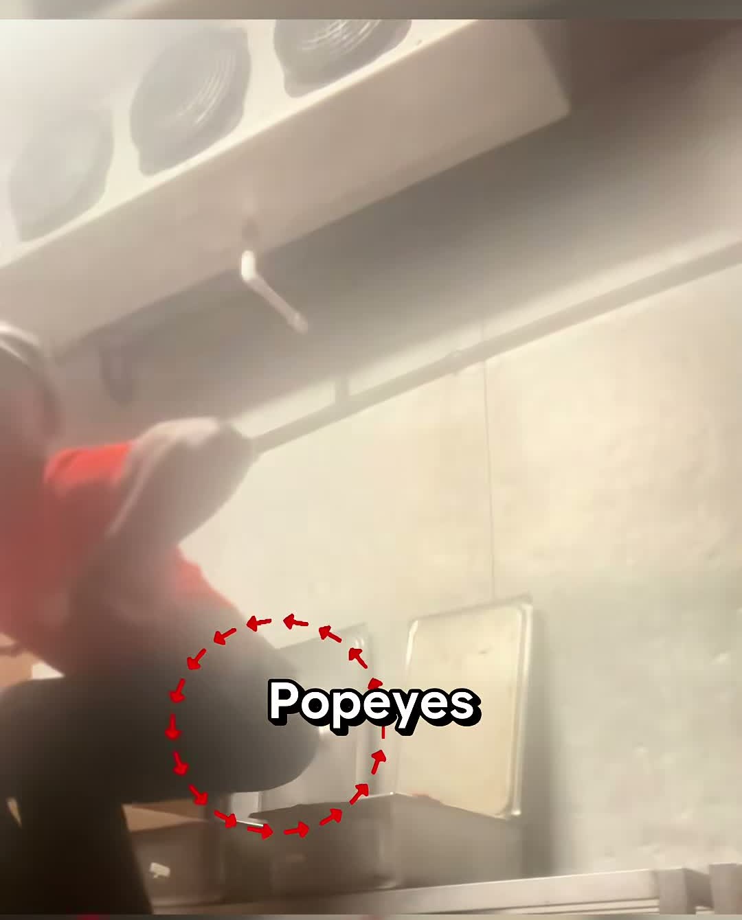 A Popeyes worker in a red shirt squats over a tray of raw chicken in the kitchen, circled in red in the original video